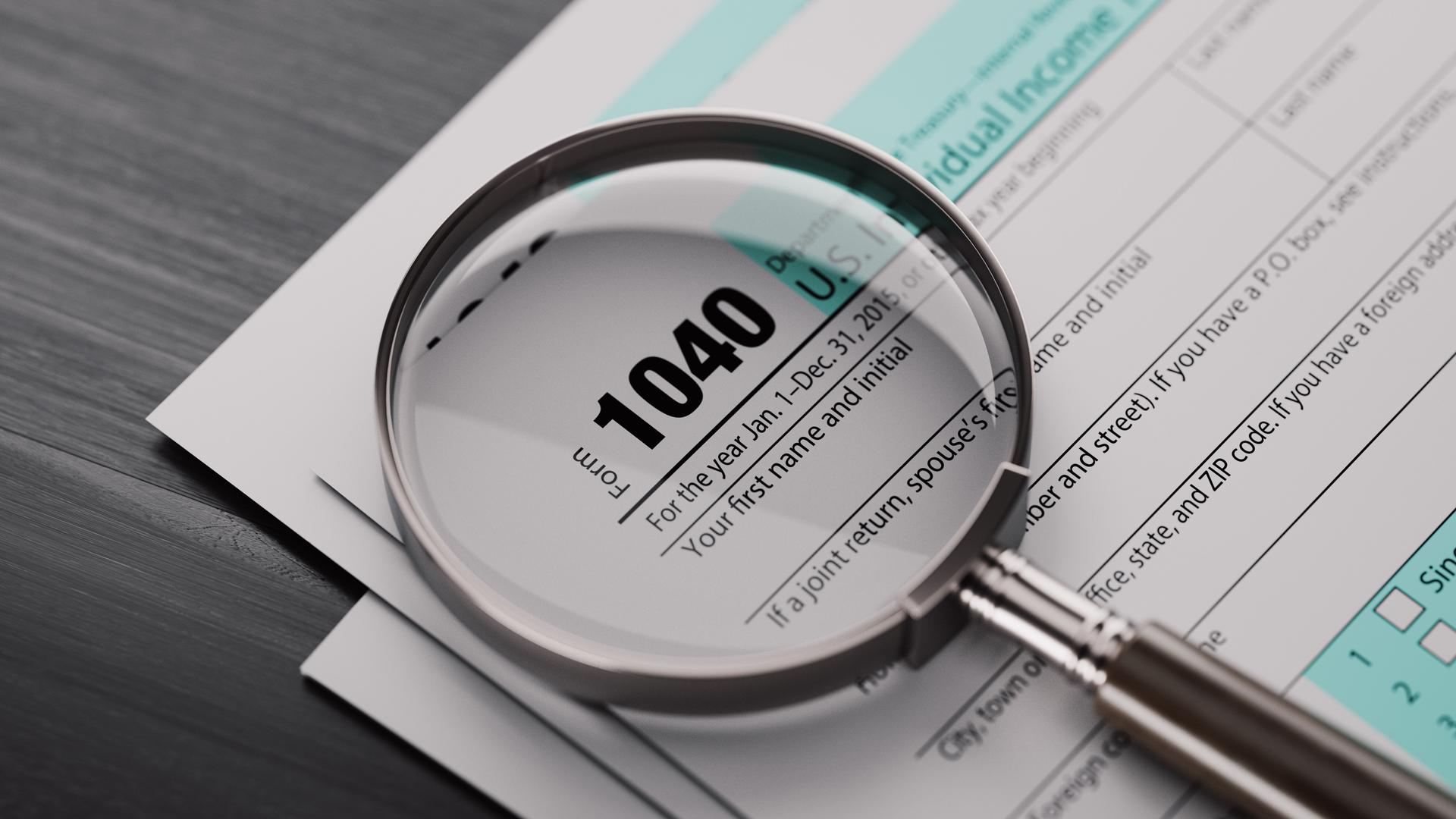 1040 Tax Form And A Magnifying Glass On Black Wood Surface